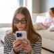 A girl chatting on her cell phone is seen from the front, with her mother seated in the background