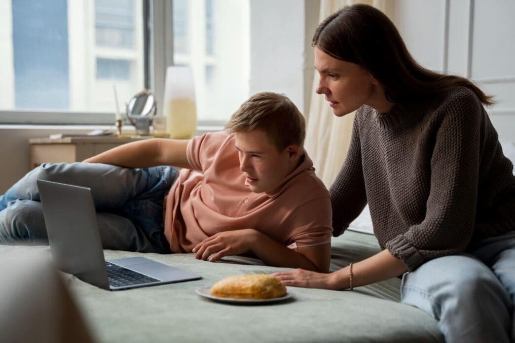 A medium shot of a boy and his mother sharing special moments together on a laptop while lying in bed