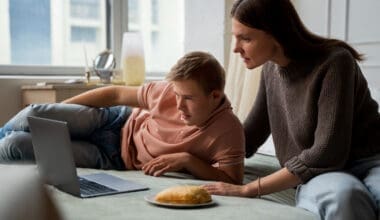 A medium shot of a boy and his mother sharing special moments together on a laptop while lying in bed