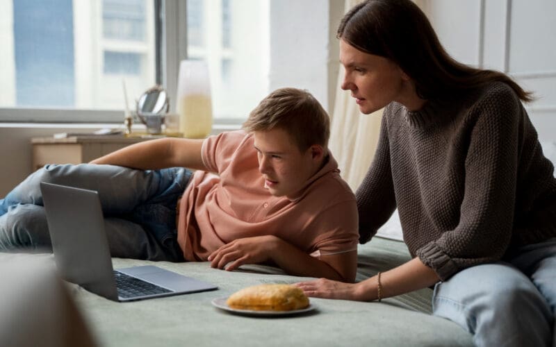 A medium shot of a boy and his mother sharing special moments together on a laptop while lying in bed