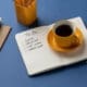 A notebook with a to-do list sits on a desk next to a cup of coffee