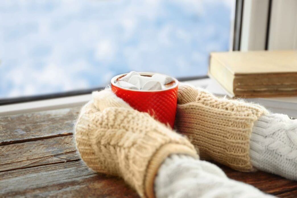 A pair of hands cradling a steaming cup of coffee on a windowsill during winter