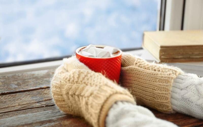 A pair of hands cradling a steaming cup of coffee on a windowsill during winter