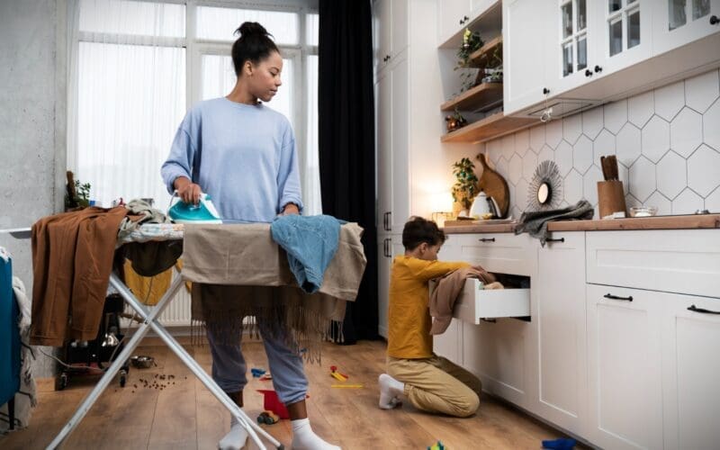 A woman is diligently cleaning a messy house while her young boy helps out, fostering teamwork and instilling habits of responsibility and cooperation in household chores