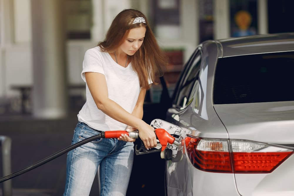 A young, beautiful woman fueling her car at a gas station