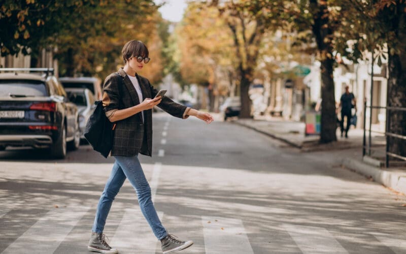 A young woman confidently crosses the road, embodying a sense of purpose and independence, her style reflecting modern trends as she navigates the bustling urban environment.