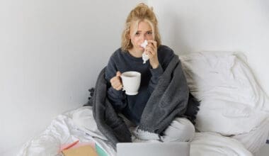 A young woman is at home feeling unwell, sipping tea and passing time in bed