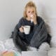 A young woman is at home feeling unwell, sipping tea and passing time in bed