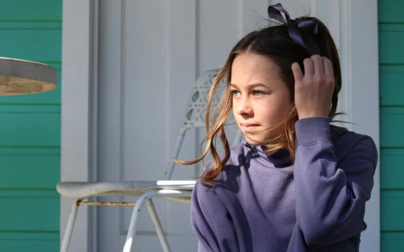 Adorable girl gazing off to the side while sitting against a door