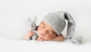 Adorable newborn peacefully sleeping in a grey crocheted hat, snuggled up with a toy rabbit