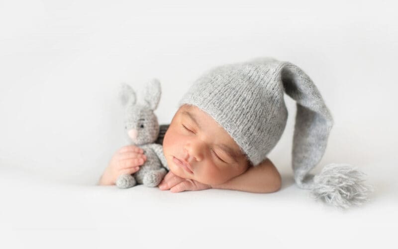 Adorable newborn peacefully sleeping in a grey crocheted hat, snuggled up with a toy rabbit