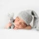 Adorable newborn peacefully sleeping in a grey crocheted hat, snuggled up with a toy rabbit