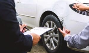 An insurance agent and a car owner assess minor damage to the vehicle's body