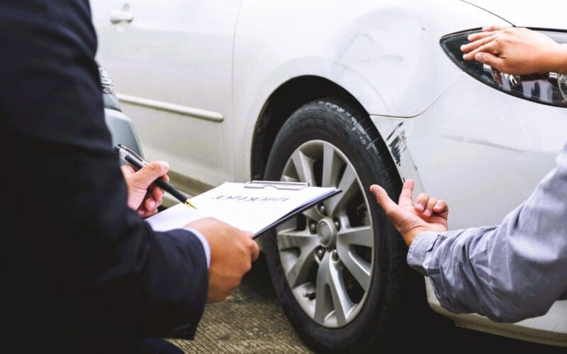 An insurance agent and a car owner assess minor damage to the vehicle's body