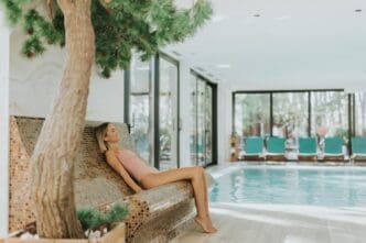 Attractive young woman unwinding by an indoor swimming pool surrounded by a natural setting featuring a tree