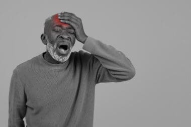 Black and white portrait of an elderly Black man featuring a bright red mark on his head, indicating an injury