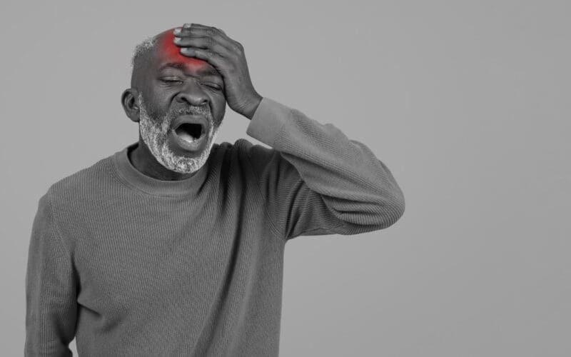 Black and white portrait of an elderly Black man featuring a bright red mark on his head, indicating an injury