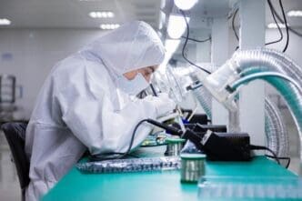 Chinese factory workers in white lab coats and face masks are seated at their stations, engaged in semiconductor production