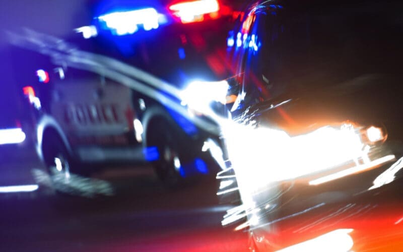 Close-up of a police car pursuit on a brightly lit street at night