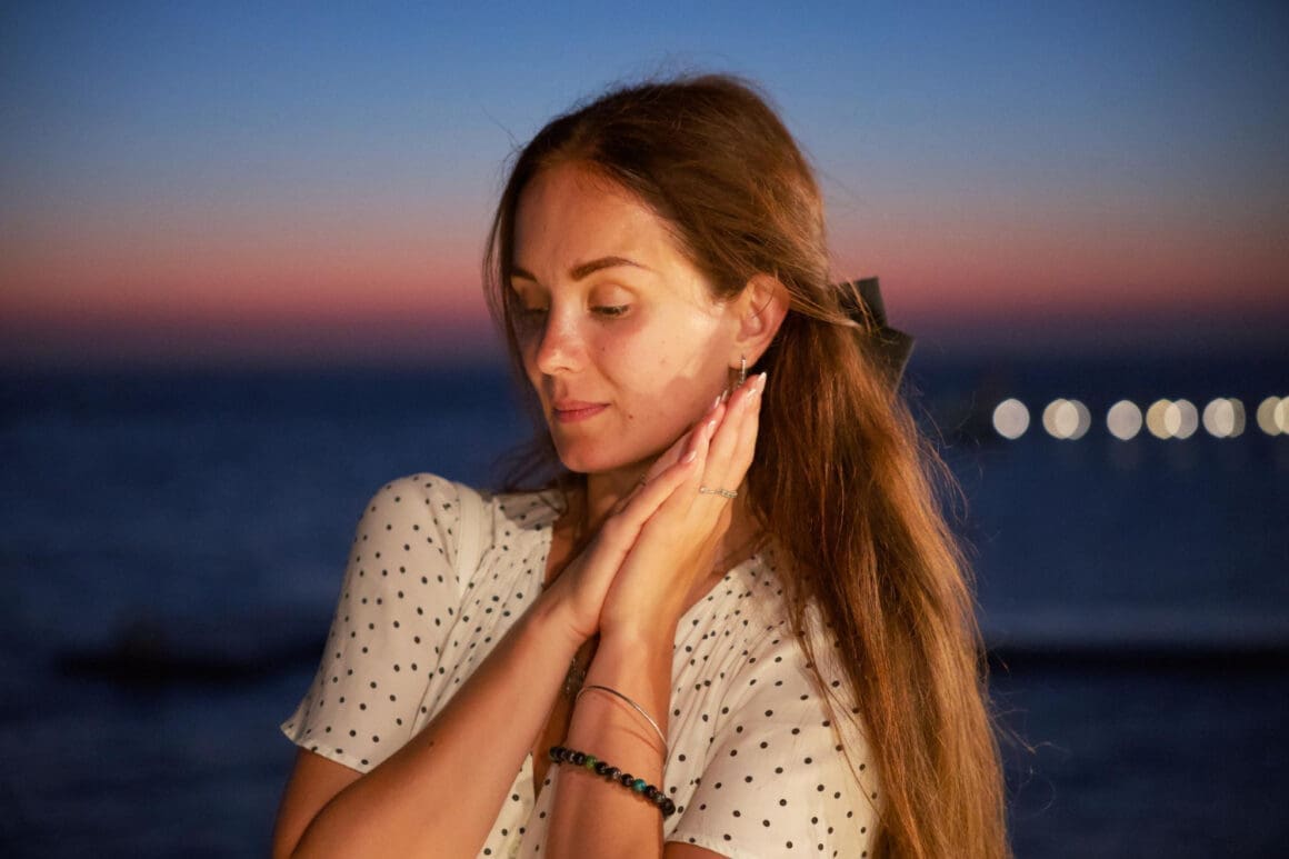 Feeling woman posing at sunset with an ocean view and gentle bokeh lights in the background