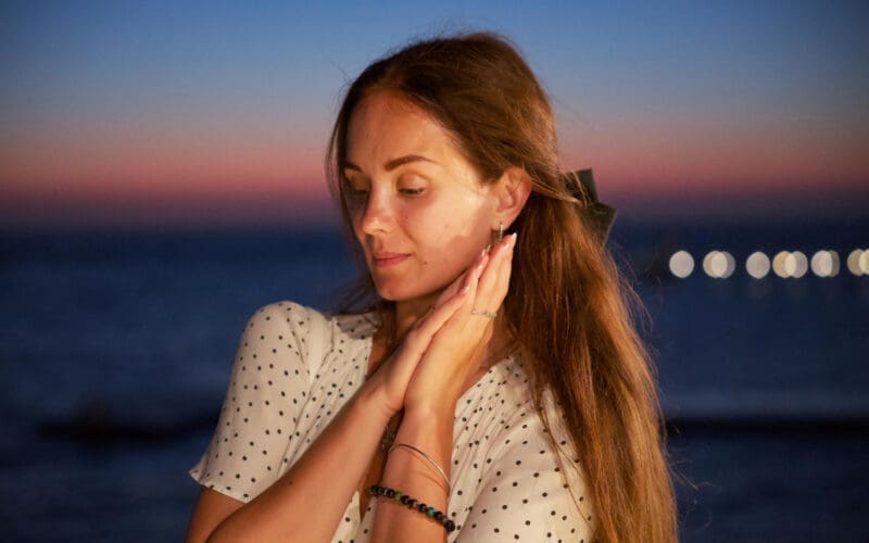 Feeling woman posing at sunset with an ocean view and gentle bokeh lights in the background