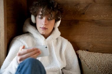 Gen Z teenager sitting on his bed, listening to music on his smartphone