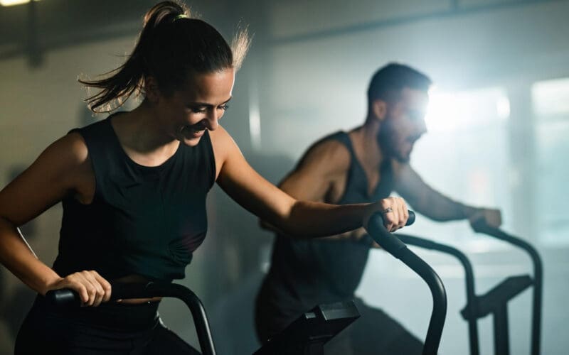 Happy couple cycling as part of their cross-training at a fitness center