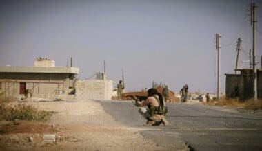 Man crouched in the road in Iraq, aiming a firearm