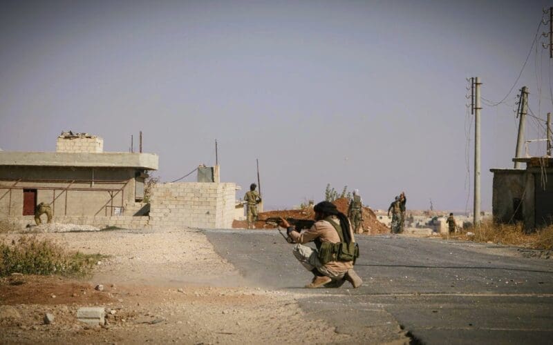 Man crouched in the road in Iraq, aiming a firearm