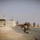 Man crouched in the road in Iraq, aiming a firearm