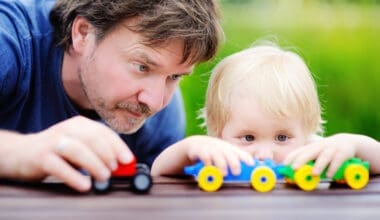 Middle age father with his toddler son playing with toy trains outdoors