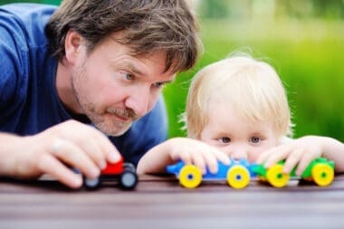 Middle age father with his toddler son playing with toy trains outdoors