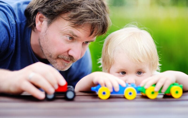 Middle age father with his toddler son playing with toy trains outdoors