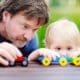 Middle age father with his toddler son playing with toy trains outdoors