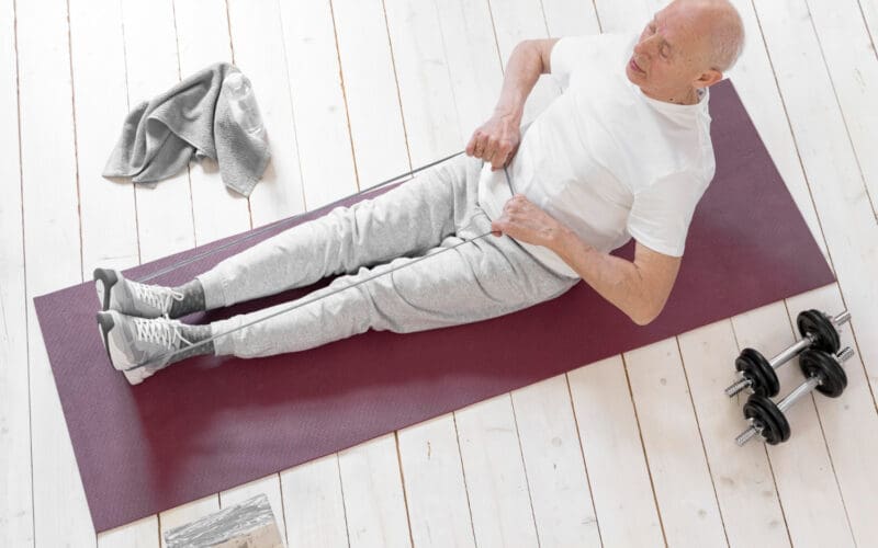 Wide shot of an elderly man exercising with a resistance band