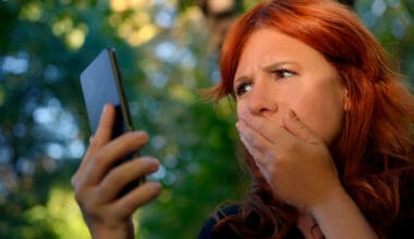 Woman outdoors covering her mouth while gazing at her cellphone screen