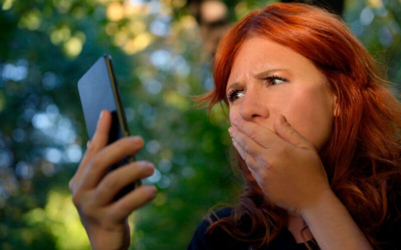 Woman outdoors covering her mouth while gazing at her cellphone screen