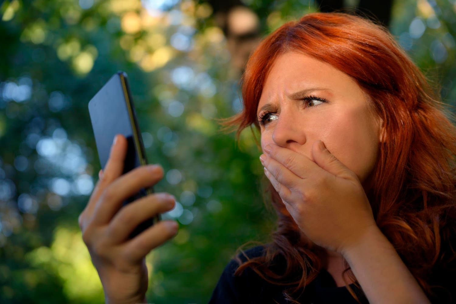 Woman outdoors covering her mouth while gazing at her cellphone screen