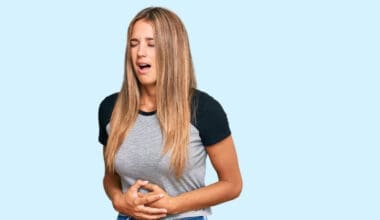 Young blonde woman wearing casual clothes with hand on stomach because nausea, painful disease feeling unwell