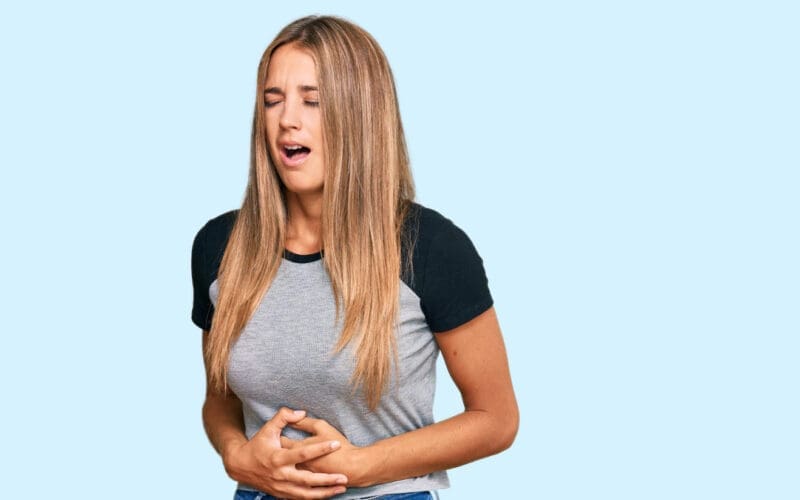 Young blonde woman wearing casual clothes with hand on stomach because nausea, painful disease feeling unwell