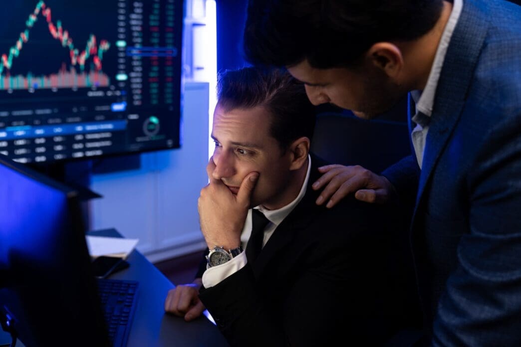 Stressful two stock investors with disappointed face focusing on dynamic currency market graph in recession stage.