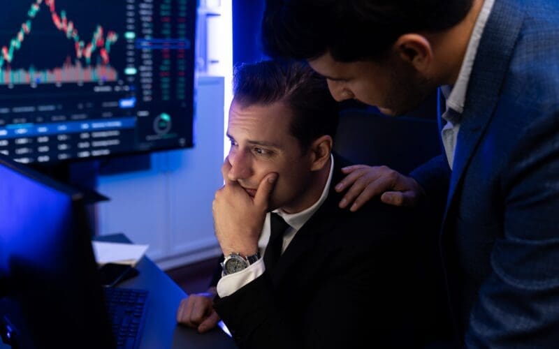 Stressful two stock investors with disappointed face focusing on dynamic currency market graph in recession stage.