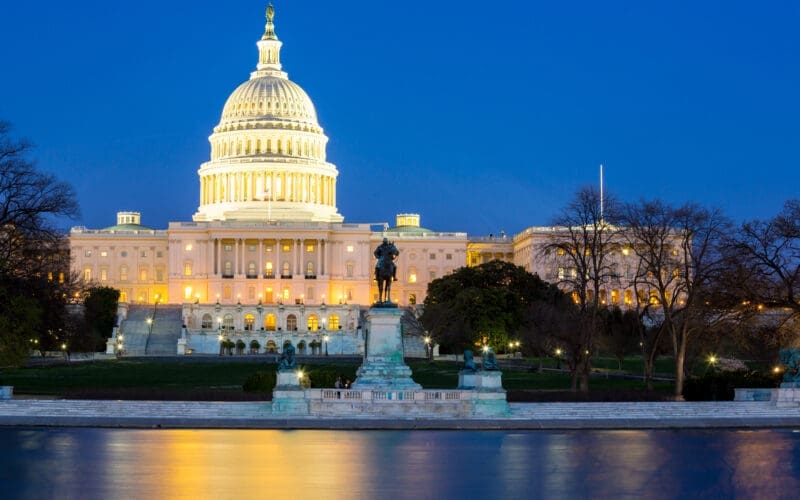 The U.S. Capitol Building in Washington, D.C., is seen at dusk, with its iconic dome and illuminated windows reflecting the fading light.