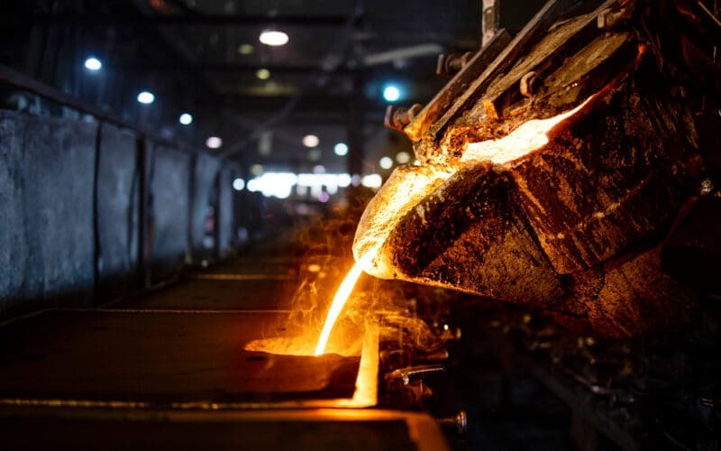 A bucket of hot molten iron is being poured into a mold during the industrial steel production process, which includes melting, molding, and foundry operations