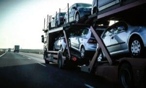 A car transport trailer filled with numerous vehicles travels along a highway