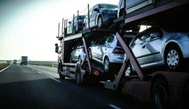 A car transport trailer filled with numerous vehicles travels along a highway