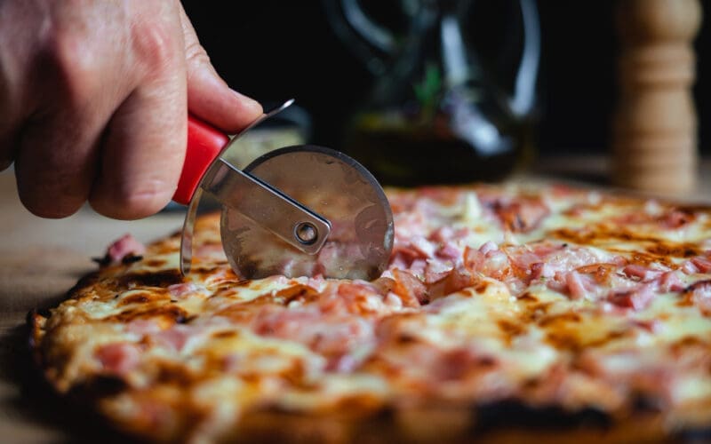 A chef slicing a pizza with a pizza cutter