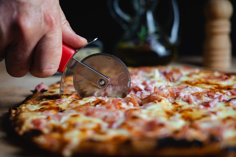 A chef slicing a pizza with a pizza cutter