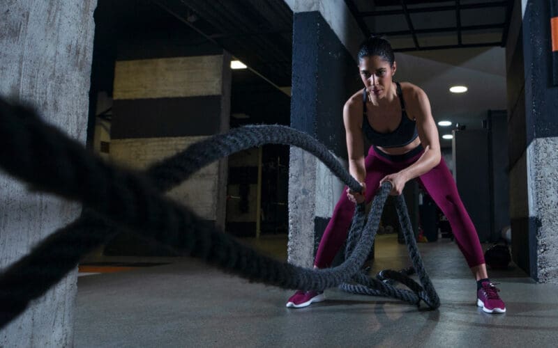 A fit woman exercising with battle ropes at the gym