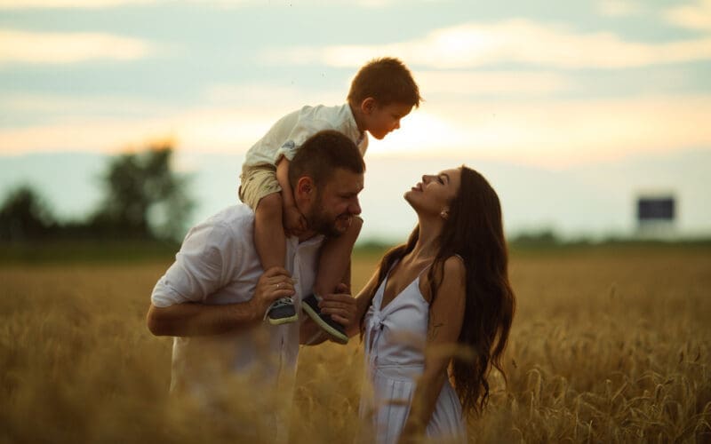 A lovely mom, dad, and their adorable little child enjoy quality time together, sharing laughter and smiles outdoors.